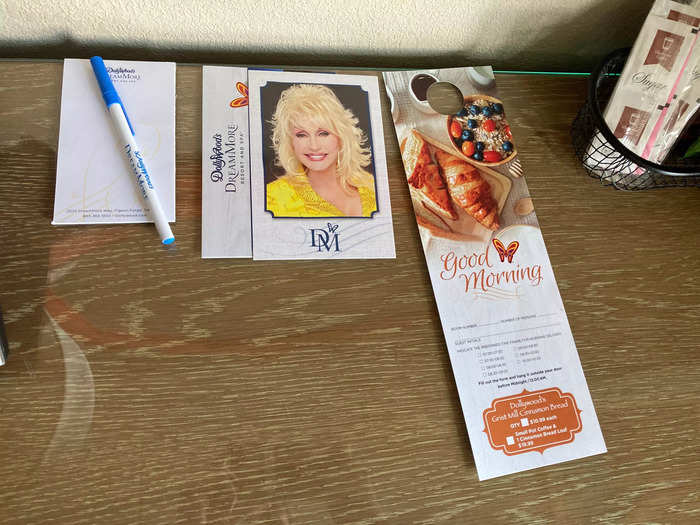 A postcard with a photo of Parton sat on the desk, in addition to the room service menu and a notepad and pen.