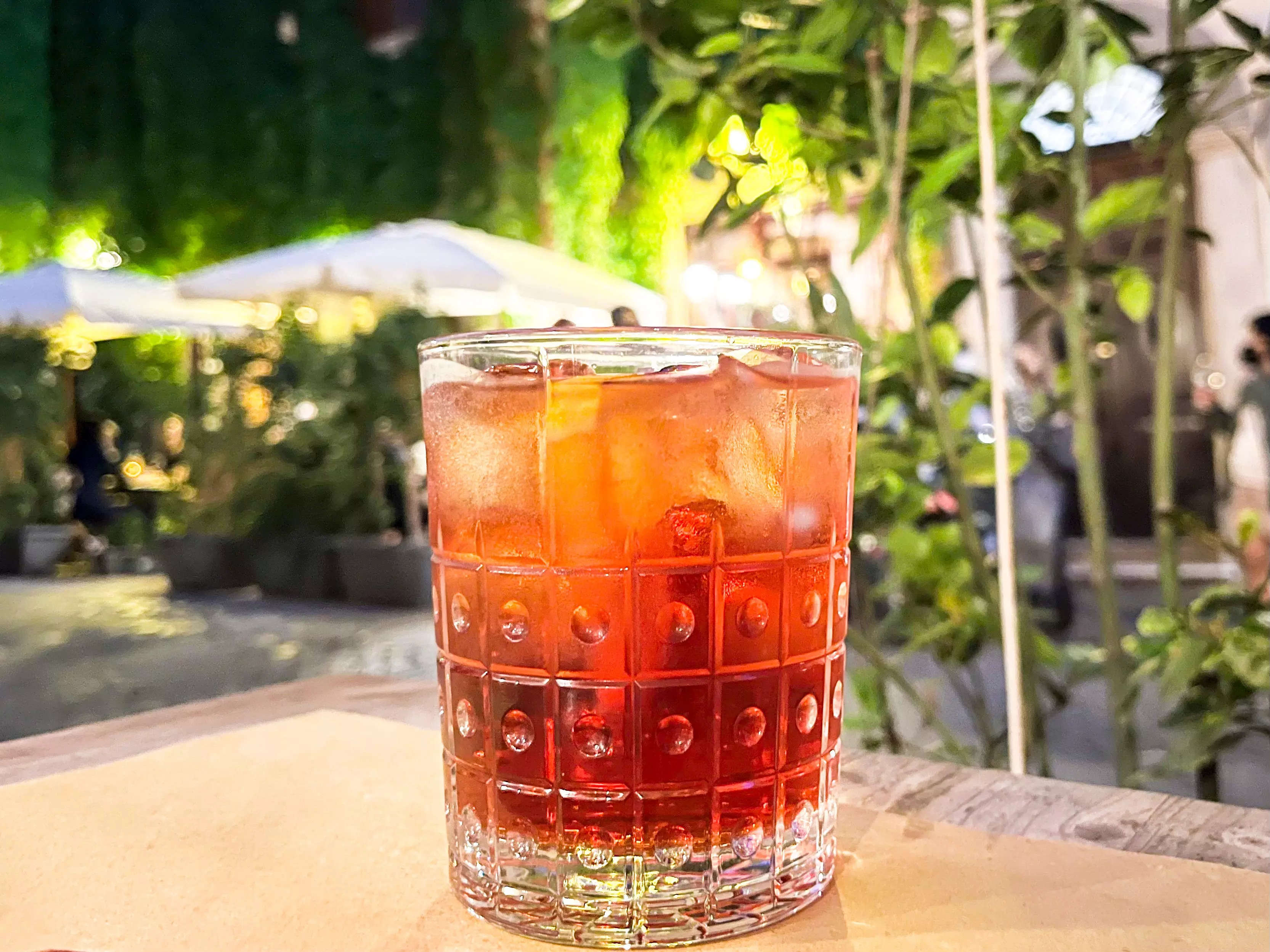 A Milano-Torino cocktail on a table in front of a vine covered building.