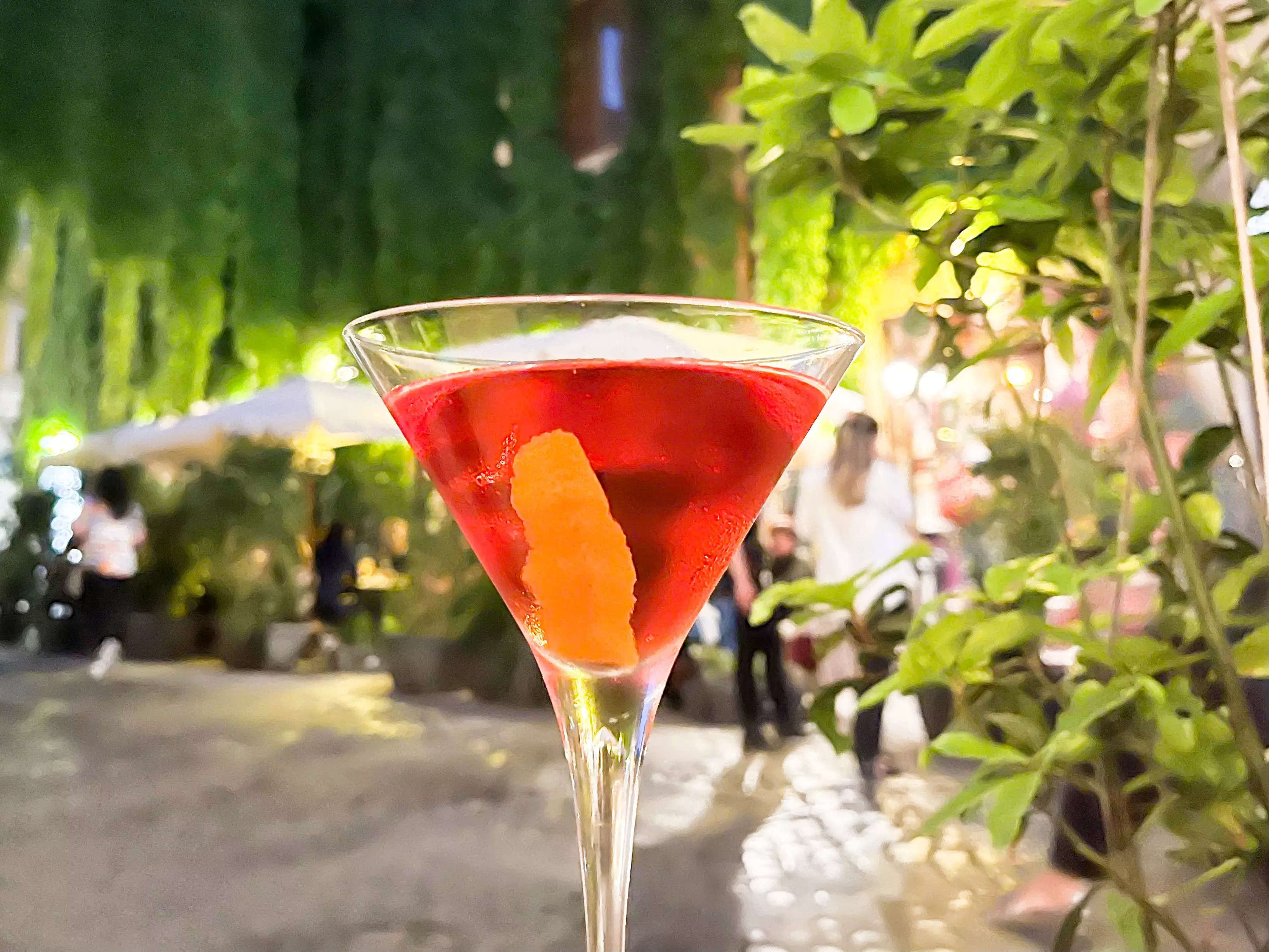 A Cardinale cocktail on a table in front of a vine covered building.