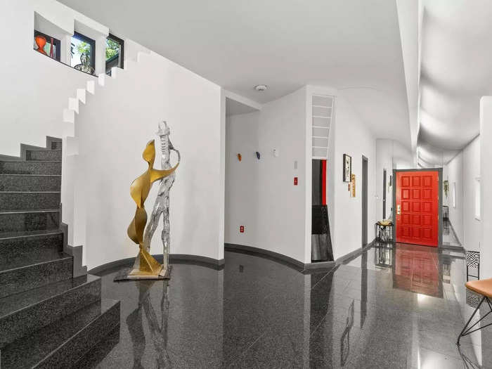 The main entrance hallway has black tiled floors and white walls, with red accents throughout. A semi-spiral staircase off the side of the hallway leads upstairs.