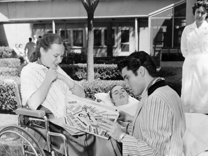 May 17, 1957: Elvis Presley meets fans with polio, looking at a scrapbook completed by Beth Currier (left), which she made using mostly her mouth.