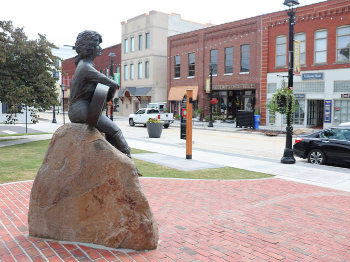 Sculpted by Jim Gray, the statue depicts Parton perched on a rock, smiling and strumming a guitar.