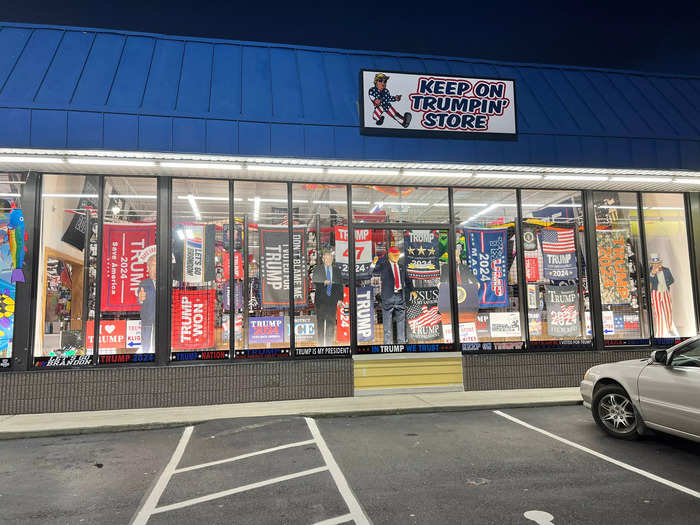 The jam-packed storefront features an animatronic mannequin of Trump waving a “Let’s Go Brandon” flag at passersby.