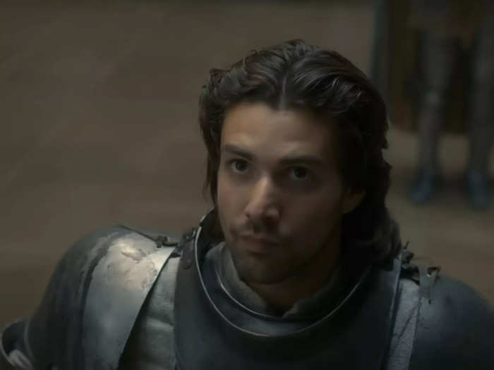 Criston Cole is young and solemn knight with curly brown locks and light facial hair.