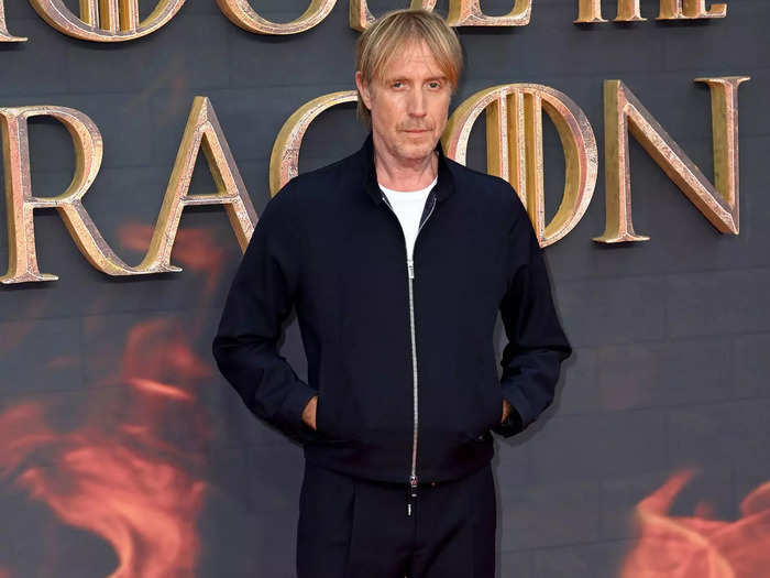 In real life, Rhys Ifans has a less thick beard and lighter hair color. His hair is also not combed over like in the show.