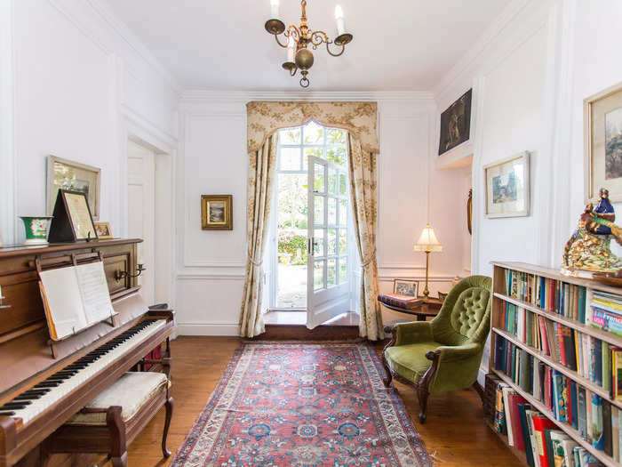 The music room has a French door that leads out into the garden, and the owner has decorated the space with a bookshelf and piano.