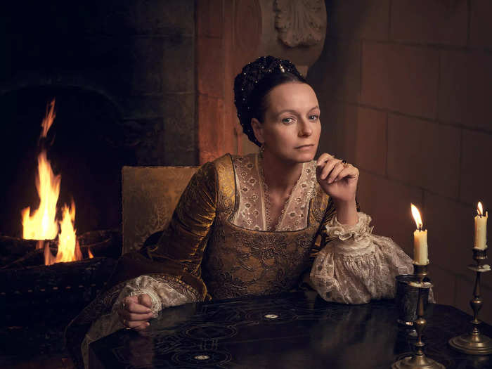 Samantha Morton plays the elder version of Queen Catherine de Medici. She wears elaborate braided hairstyles and jewel-toned dresses with lace collars and puffed sleeves.