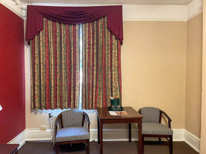 Two chairs and a table sat against a wall and a window overlooked an adjacent building.