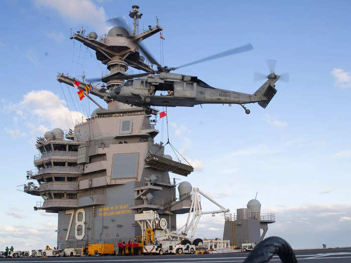 An MH-60S Nighthawk helicopter lands on the flight deck of USS Gerald R. Ford. Behind is the flight command center or the ship