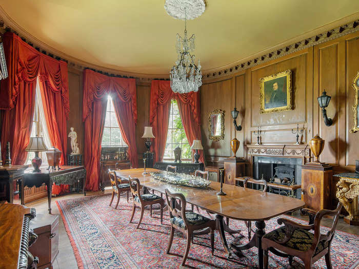 The dining room is decorated with red curtains and an oil painting that hangs over the fireplace. The room offers plenty of space for dinner parties and family gatherings alike.