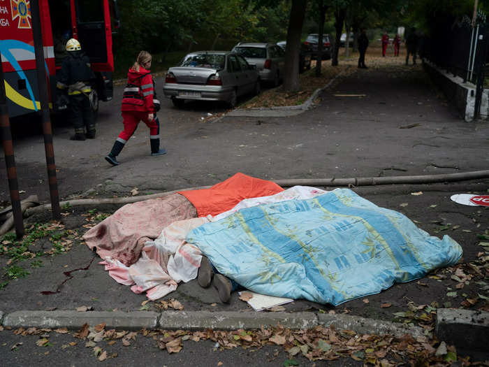 A rescue service member walks by three bodies covered by blankets in Dnipro.