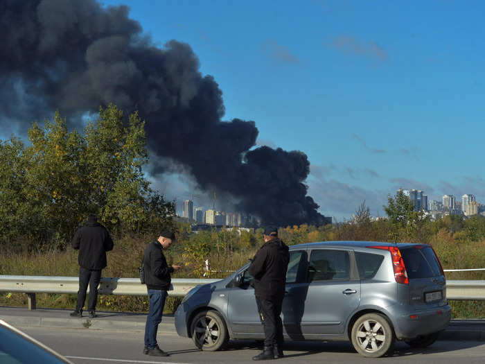 Bystanders in Kyiv watch as smoke rises over the city after a missile strike.