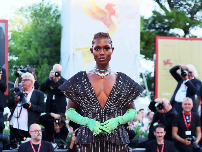 Turner-Smith was draped in a red and black plunging Gucci dress, with green elbow-length gloves at the August 2022 "White Noise" premiere in Venice.