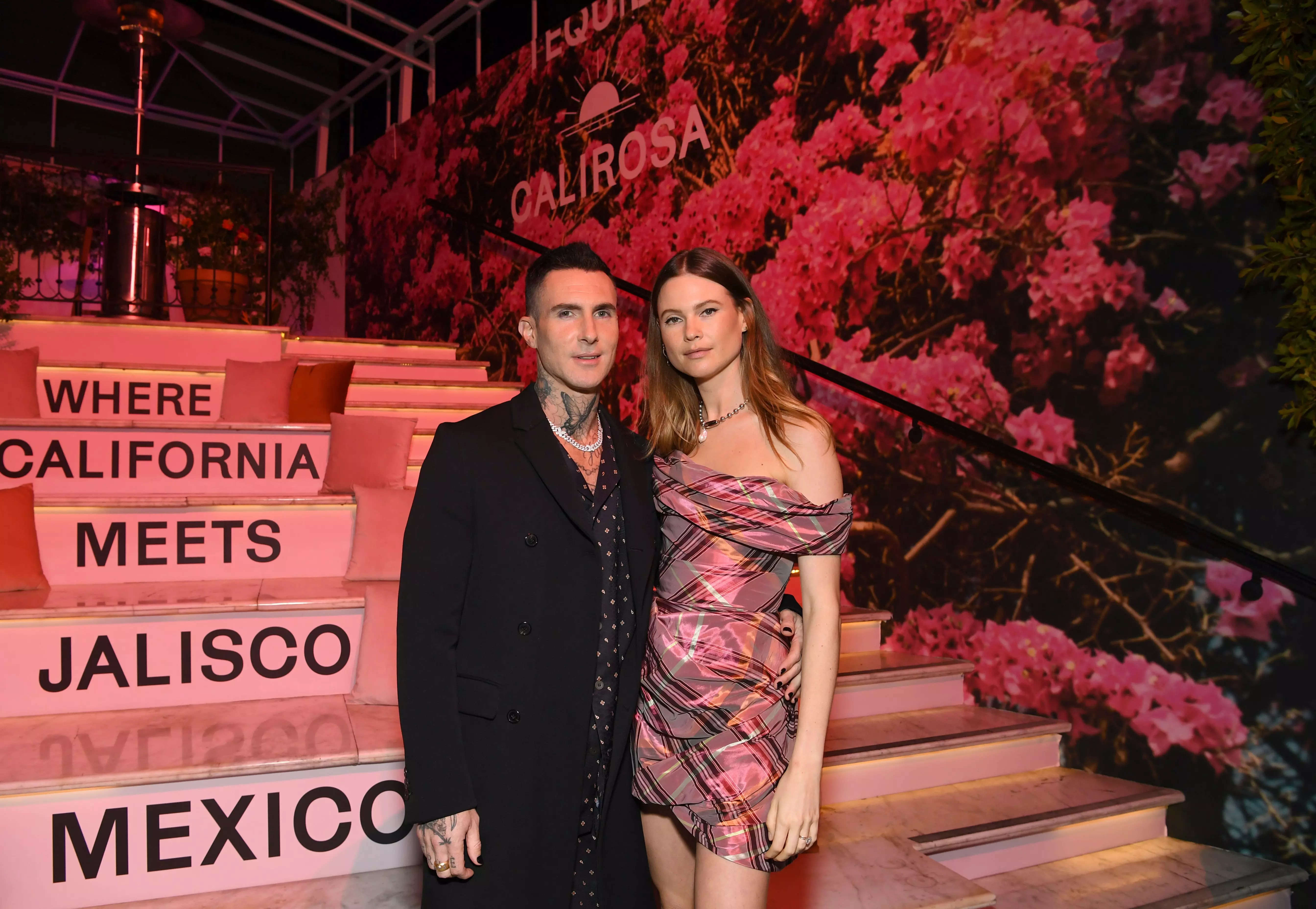 Marron 5 frontman Adam Levine in a black suit next to his wife, model Behati Prinsloo, in a pattern minidress