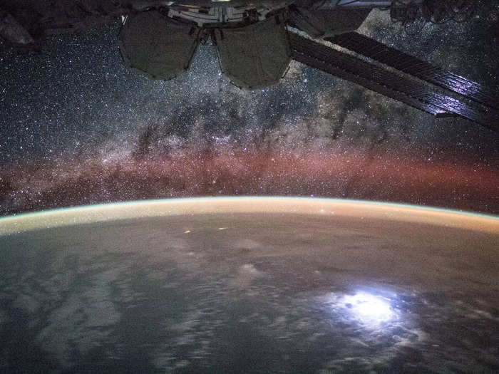 At night, astronauts can catch a stunning view of the Milky Way stretching above them. In this photo, a lightning bolt flashes on Earth below.