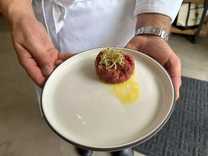 Massarweh holds a plate of grass-fed steak tartare made from filet mignon, quail egg, and broccoli sprouts. Purchased à la carte, it costs $32.