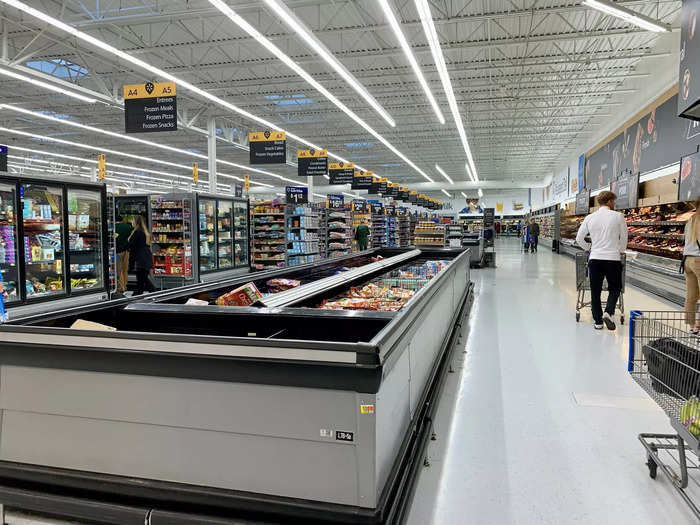 The back wall is made up of meats and cheeses on refrigerated shelves, with frozen foods on display in the middle of aisles.