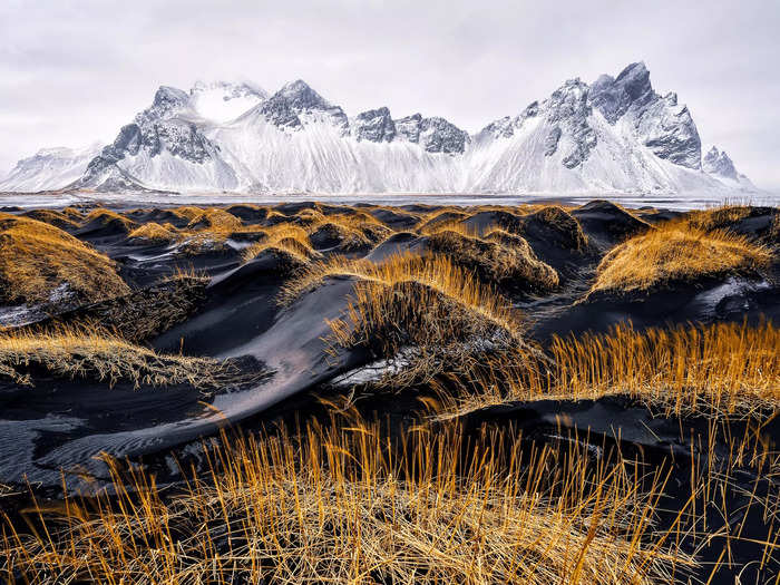 Snowy mountains stand in stark contrast against a black sand beach in Iceland.