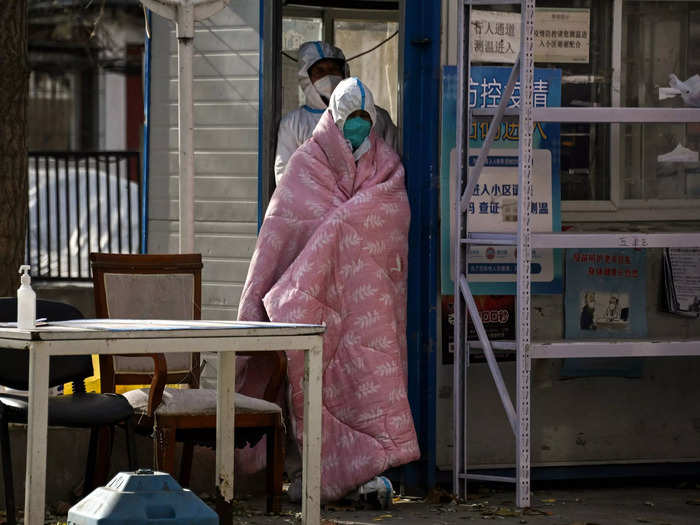 A worker in personal protective equipment stands by the entrance of a residential area in Beijing that