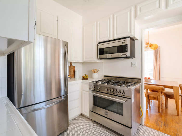 The dining area leads into an all-white kitchen with stainless steel appliances.