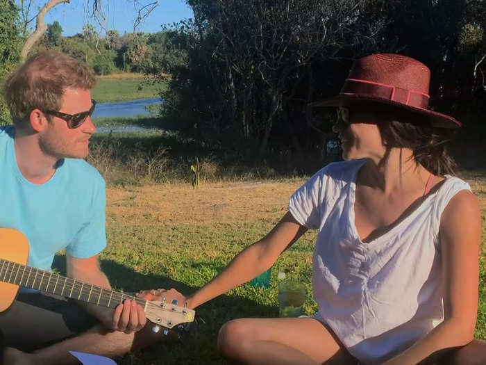 Harry plays guitar as he sits with Meghan outside at an undisclosed location.