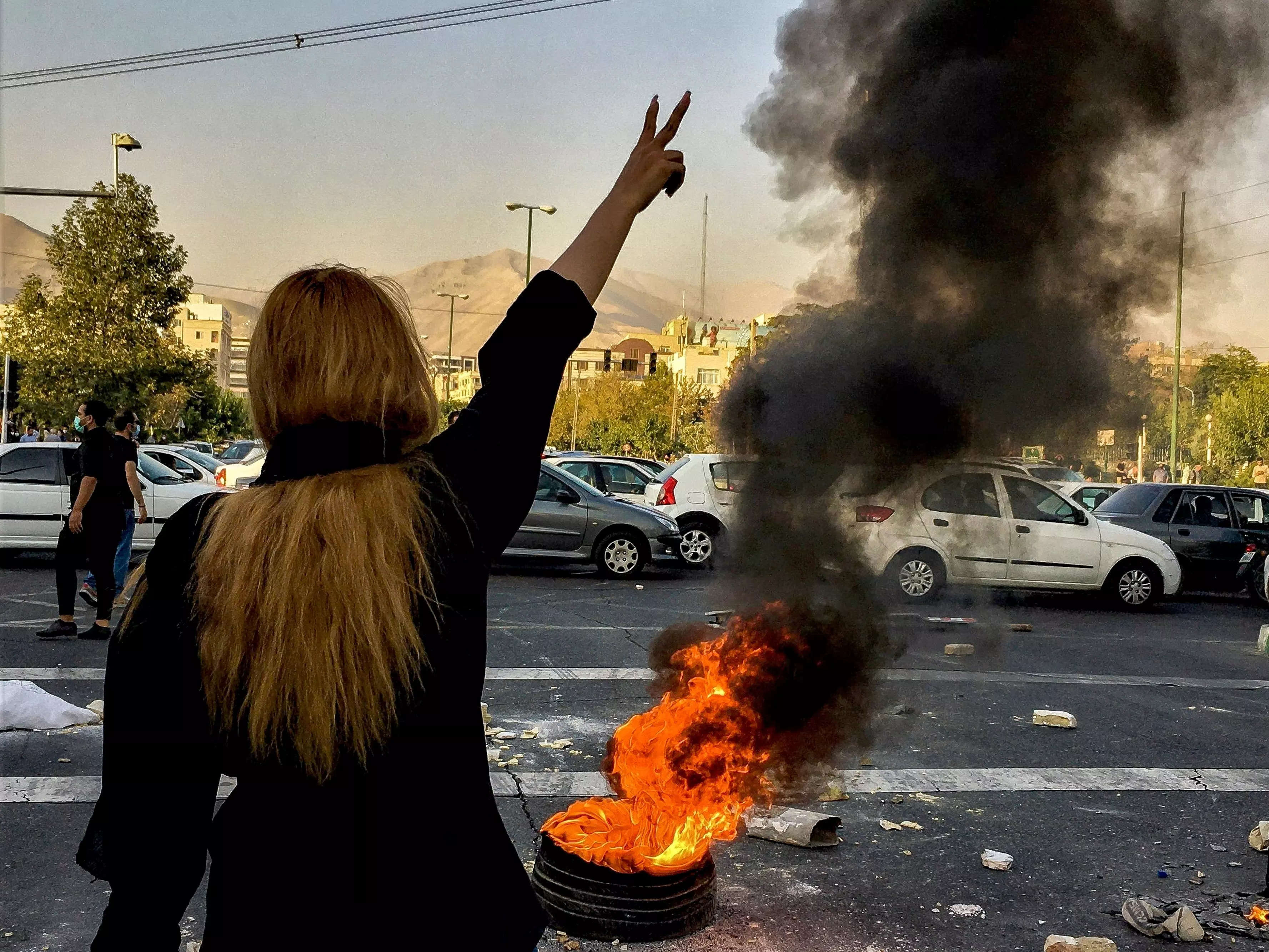 A woman holds up a "V" sign in front of a small fire during a protest in Iran.