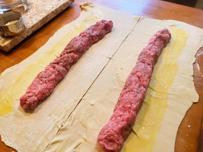 After I pulled the two logs of sausage meat from the fridge, I placed them on top of the sheets and brushed one long side of each rectangle with beaten egg.