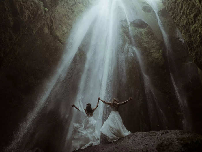 Two brides were photographed next to an Icelandic waterfall — the water almost looks like streaks of sunlight.