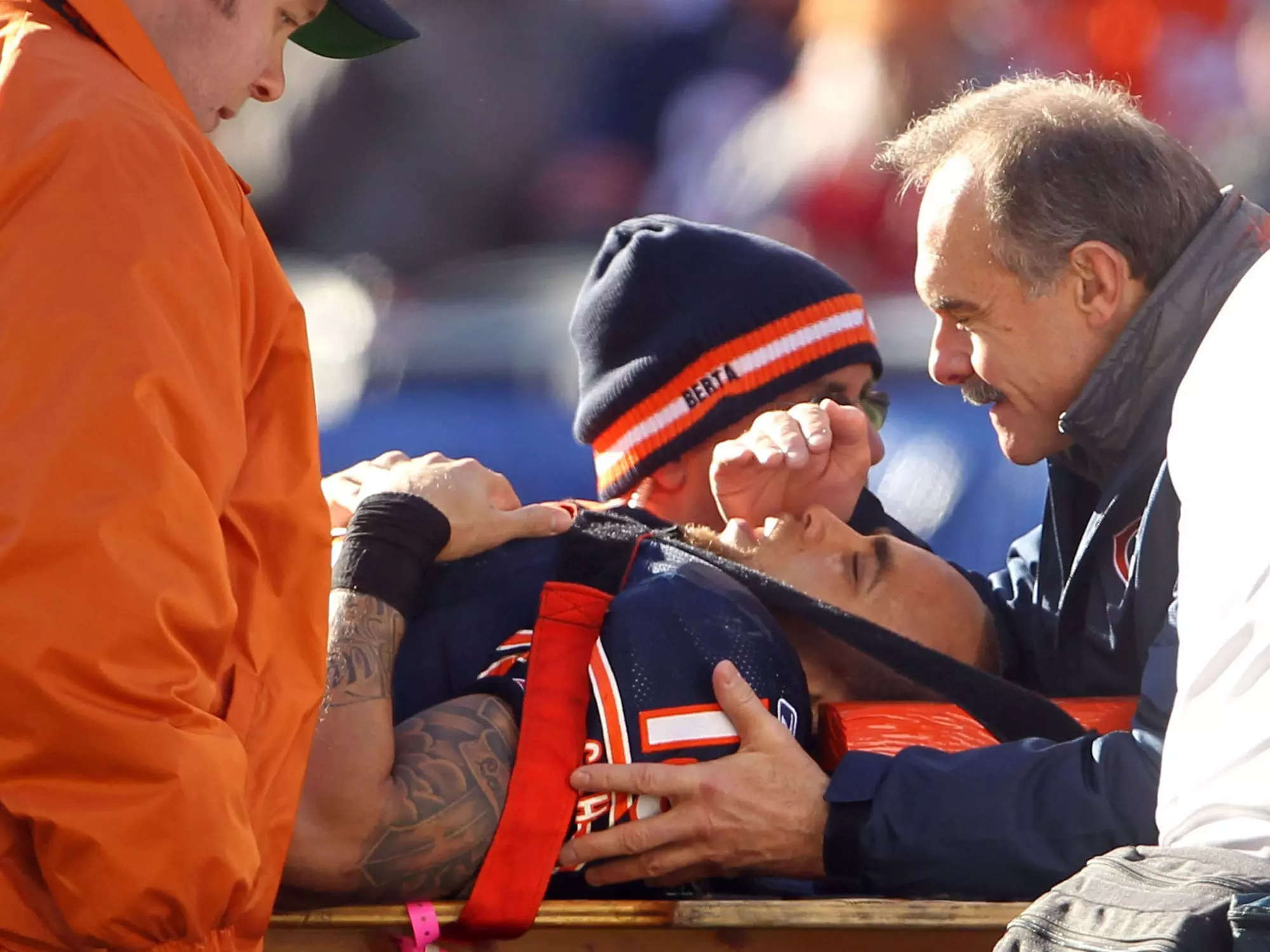 Johnny Knox is seen surrounded by medical staff while laying on a stretcher. He has a pained expression on his face.
