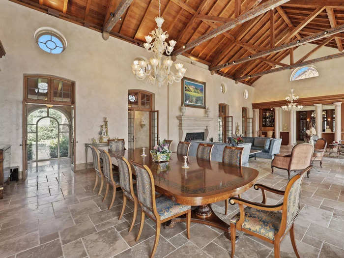 The kitchen leads into the living area, which has a magnificent chandelier, wooden beams, and tiled flooring.