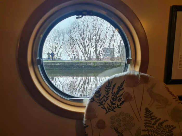 The houseboat has circular windows that look out onto the canal, with glimpses of the city skyline.