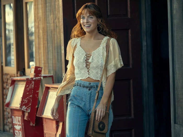 Daisy Jones, the free-spirited lead singer of the band, is played by Riley Keough. Her hair is copper red and in flashbacks to the 1970s, she wears eclectic outfits that are fitting for the era.