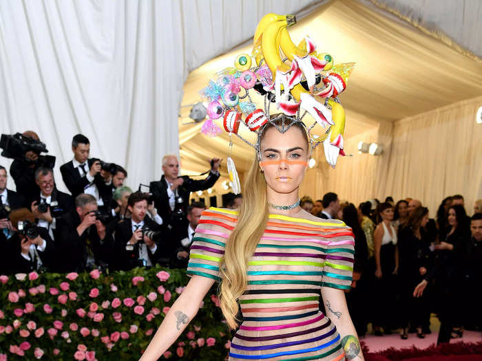 For the Met in 2019, Delevingne wore a rainbow-striped jumpsuit with a sculptural headpiece featuring a bunch of bananas, chattering teeth, and more.