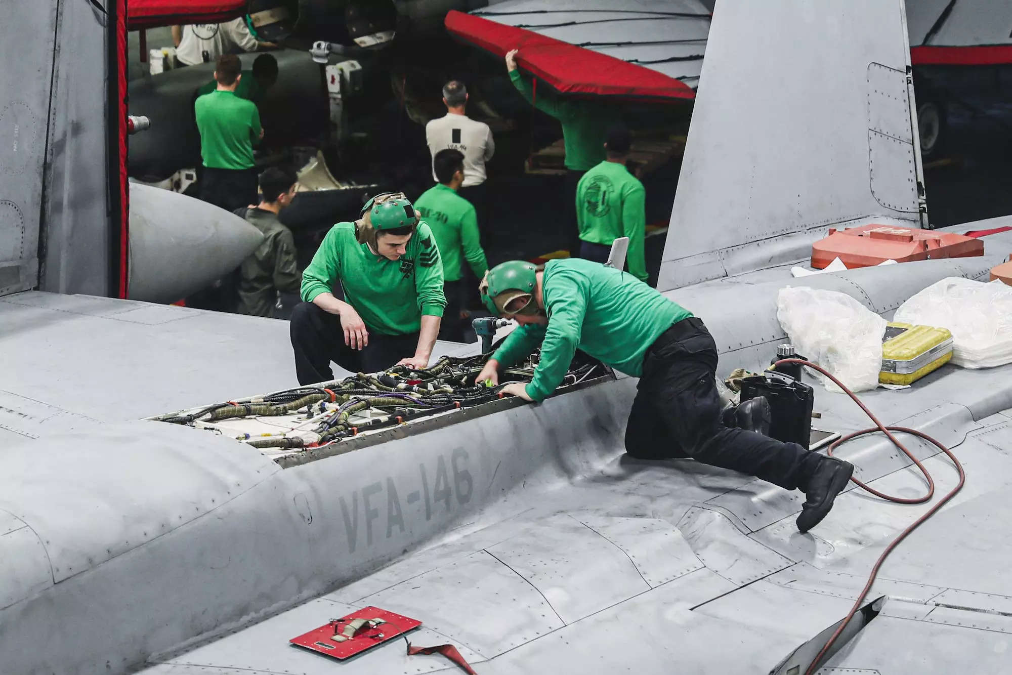 Two US Navy maintainers performing maintenance on a F/A-18E Super Hornet.