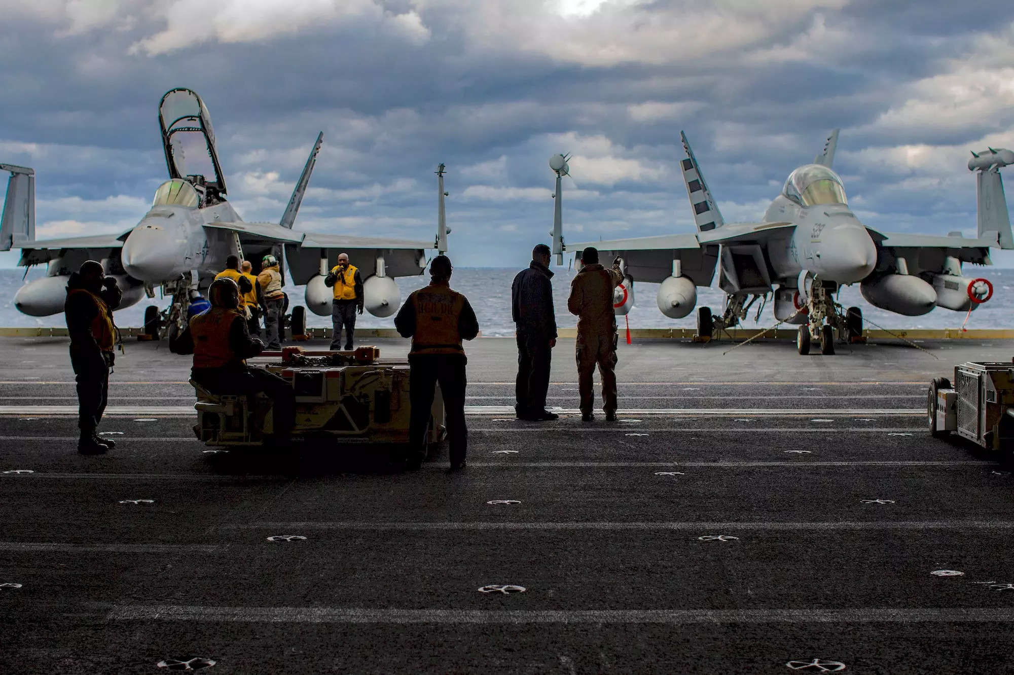 US Navy personal looking at an F/A-18F Super Hornet and a E/A-18G Growler on an aircraft elevator.