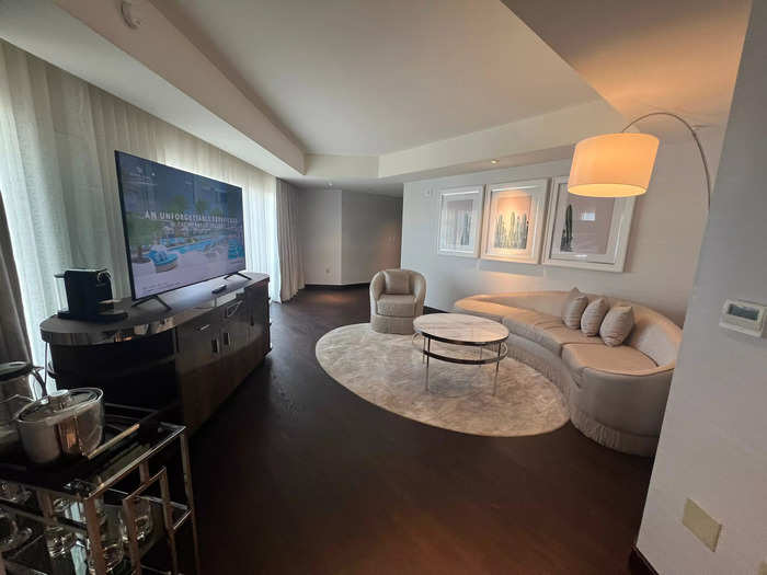 The spacious living room included a curved couch, an armchair, a bar area, and a flat-screen TV in front of a wall of floor-to-ceiling windows.