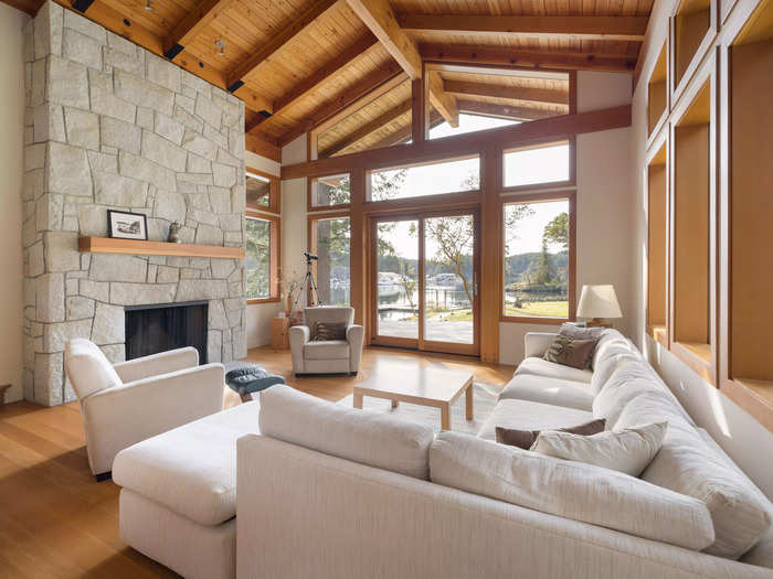 Inside, the open-concept living room features a floor-to-ceiling stone fireplace, wooden beam ceilings, and views of the surrounding waters.