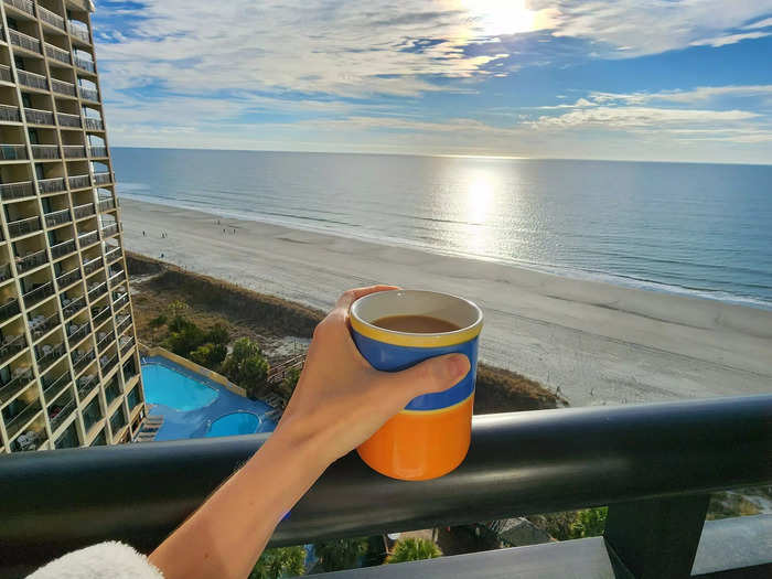 a woman holds up a cup of coffee over the ocean