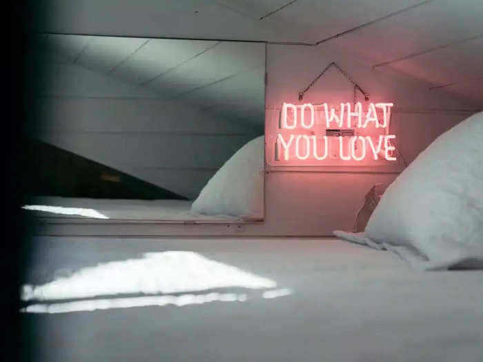 The wall by the bed is decorated with a mirror and a neon sign that says, "Do what you love."